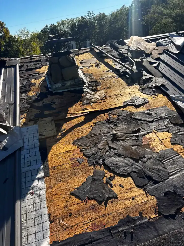 Old shingles torn off to expose weathered plank decking around a stone chimney during a roof replacement