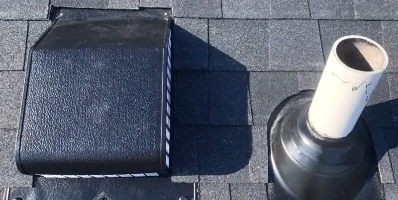 Close-up of a roof vent and a rubber pipe boot sealing a plumbing vent pipe through asphalt shingles