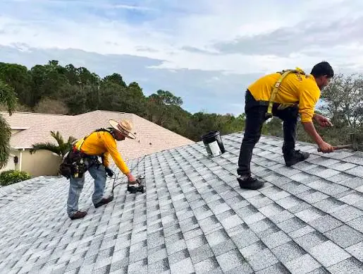 Two roofing contractors wearing safety harnesses carrying out repairs on an asphalt shingle roof