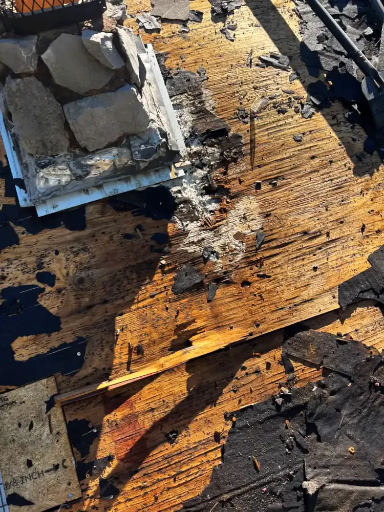 Rotted roof decking and failed flashing at the base of a stone chimney where water has been getting in